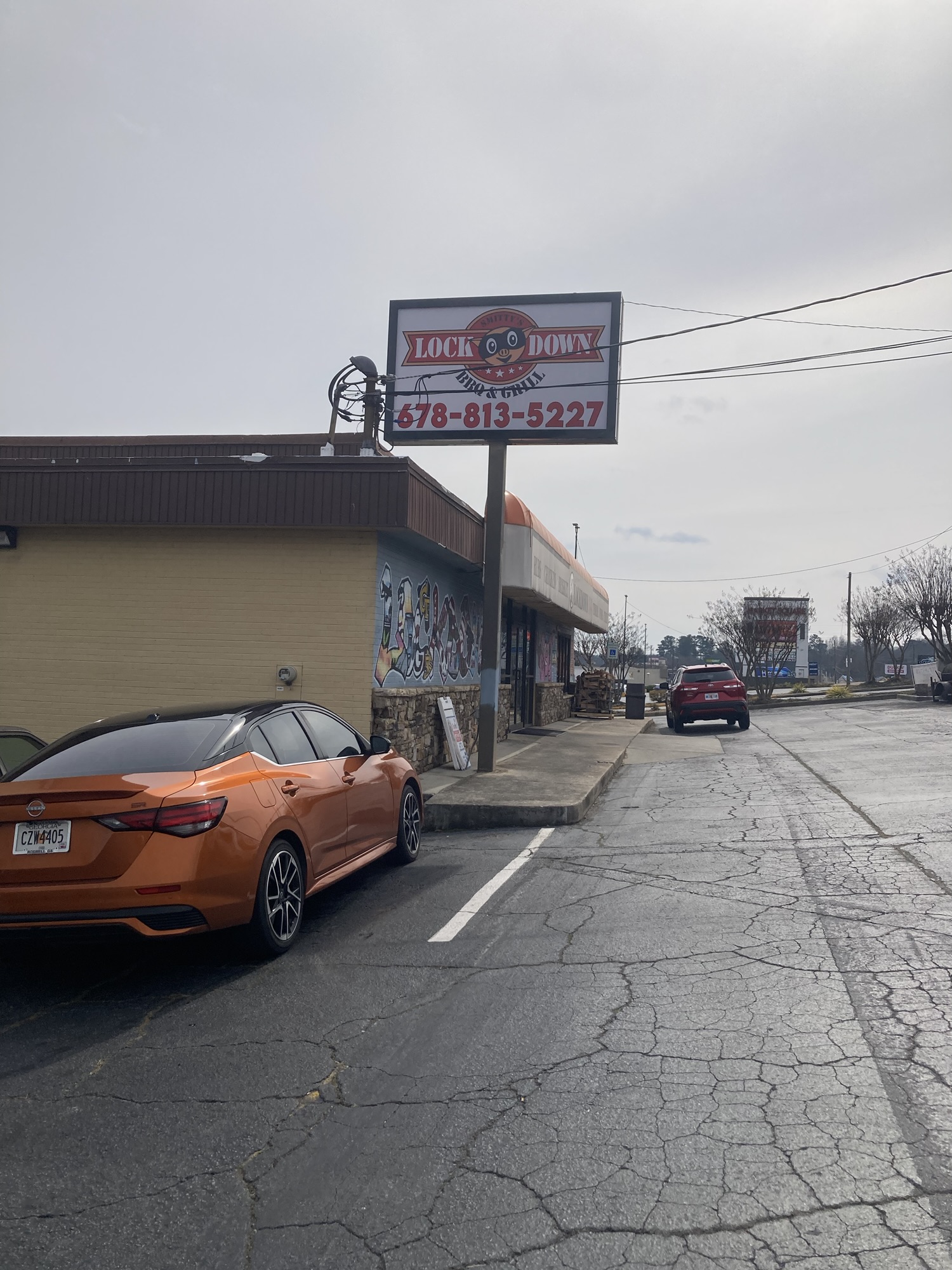 A restaurant is seen from the parking lot. The sign says Lockdown BBQ. It's a cloudy day.
