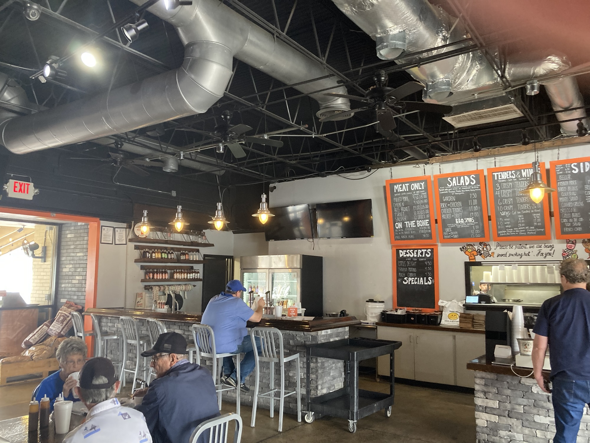 The interior of the restaurant is seen with unfinished ceiling showing pipes. The front counter can also be seen in the background.